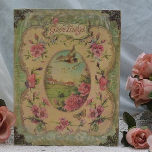 May include: A vintage-style greeting card with a green and gold frame. The card features a floral design with a bird in flight and the word "Greetings" at the top.