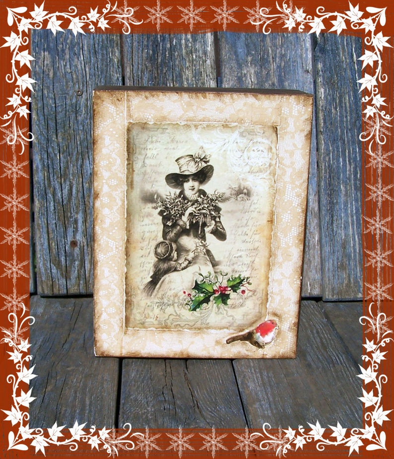 May include: A framed vintage image of a woman in a hat holding a bouquet of flowers. The frame is decorated with white lace and a small red bird is perched on the bottom.