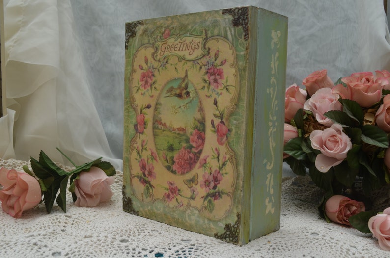 May include: A vintage-style wooden box with a floral design and the word "Greetings" on the front. The box is painted in shades of green and blue and features a bird and flowers.