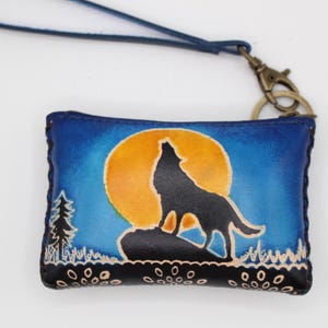 May include: A small blue leather coin purse with a wolf howling at the moon design. The purse has a zipper closure and a metal key ring.