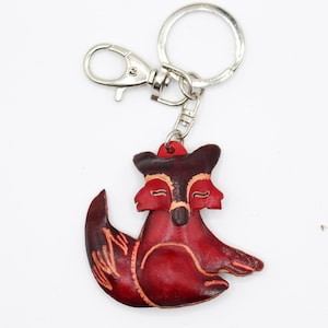May include: A red leather fox keychain with a silver key ring and a lobster clasp. The fox has a brown face and closed eyes.