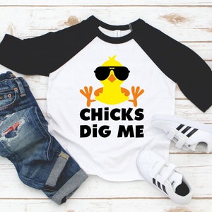 Peut inclure: Un t-shirt de baseball blanc et noir avec un poussin jaune portant des lunettes de soleil et le texte "CHICKS DIG ME".