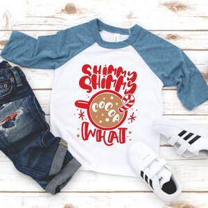 May include: A white and blue baseball tee shirt with red text that says "Shimmy Shimmy Cocoa What". The shirt features a brown mug with a candy cane and a white background.