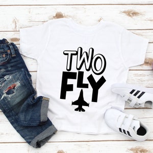 May include: White t-shirt with black text that says "TWO FLY" and a black silhouette of a jet plane.