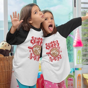 May include: Two children wearing white and black baseball shirts with the text "Shimmer Shimmer Cocoa What" and a red and brown cocoa mug graphic. The children are smiling and looking at the camera.