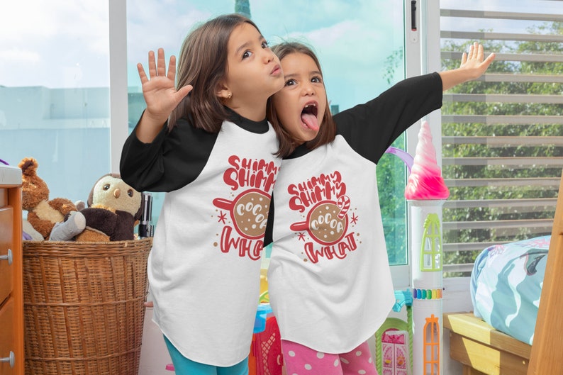 May include: Two children wearing white and black baseball shirts with the text "Shimmer Shimmer Cocoa What" and a red and brown cocoa mug graphic. The children are smiling and looking at the camera.