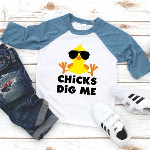 Peut inclure: Un t-shirt de baseball blanc et bleu avec un poussin jaune portant des lunettes de soleil et le texte "CHICKS DIG ME".