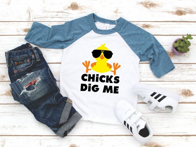 Peut inclure: Un t-shirt de baseball blanc et bleu avec un poussin jaune portant des lunettes de soleil et le texte "CHICKS DIG ME".