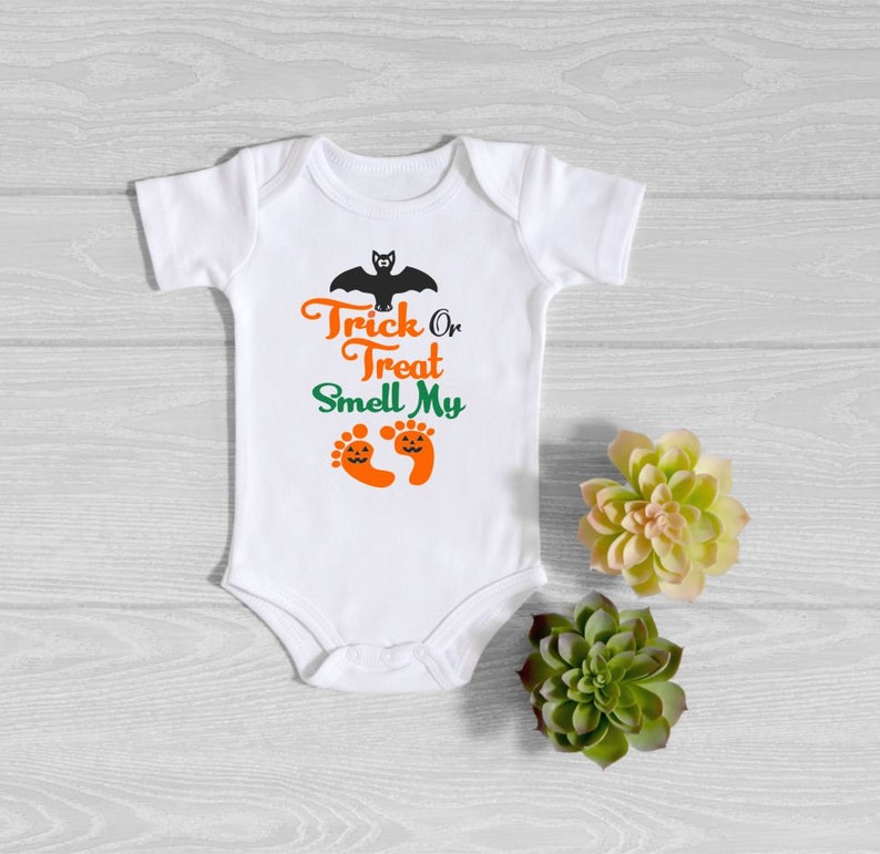 May include: White baby onesie with the text "Trick or Treat Smell My" and a black bat above the text. Two orange and green pumpkin-shaped footprints are below the text.