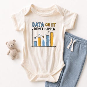 May include: Cream-colored baby onesie with the text "DATA OR IT DIDN'T HAPPEN" above a bar graph illustration in blue and yellow. A pair of blue pants with a drawstring and a small teddy bear are next to the onesie.