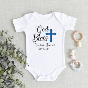May include: White baby onesie with the text "God Bless Canton James 09/17/21" and a blue cross.