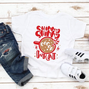 May include: White t-shirt with red text that says "Shimmer Shimmer What" and a brown mug with the word "Cocoa" and a candy cane.