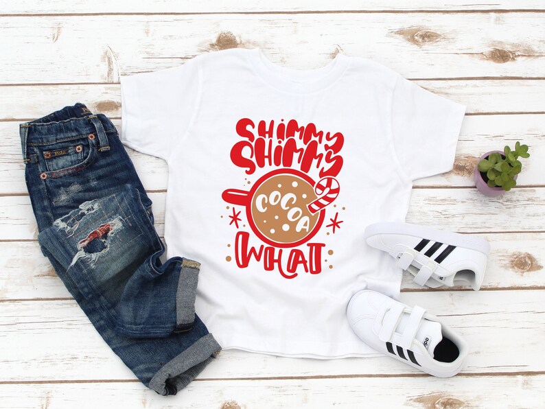 May include: White t-shirt with red text that says "Shimmer Shimmer What" and a brown mug with the word "Cocoa" and a candy cane.