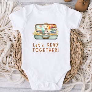 May include: White baby onesie with a watercolor illustration of a rabbit peeking out of an open suitcase filled with books. The text "Let's Read Together!" is printed in orange below the suitcase.