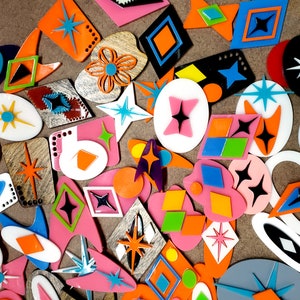 May include: A collection of colorful, geometric shapes made of acrylic. The shapes include stars, diamonds, and circles. The shapes are arranged in a random pattern on a brown background.