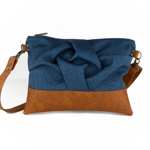 small blue crossbody bag with hand-smocked pleated detail and brown vegan leather bottom and adjustable strap; front view