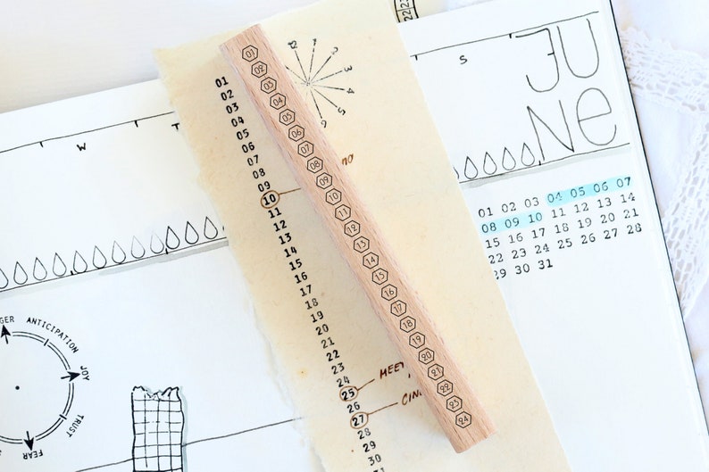 May include: A wooden stamp with a hexagonal design and numbers 1 through 31 printed on it. The stamp is used for marking dates on a calendar.