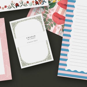 May include: A stack of notecards with a decorative border and the text "EMADAM ART & DESIGN". Other stationery items include floral and geometric patterned paper in pink, blue, and white. The notecards are 300g/ml.