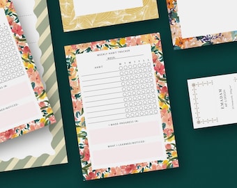 May include: A collection of floral-themed stationery items, including habit trackers and notepads. The habit tracker features a pink and floral border with spaces for tracking daily habits. The stationery has a watercolor floral design with pink, orange, and yellow flowers.