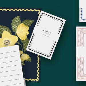 May include: White notecards with a black geometric border and the text "EMADAM ART & DESIGN" on a white band. The cards are on a dark green background with floral and lined paper elements.