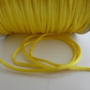 Può includere: Un rotolo di cordoncino o spago giallo brillante. Il cordoncino è avvolto strettamente attorno a un rotolo di cartone. Il cordoncino è liscio e lucido.