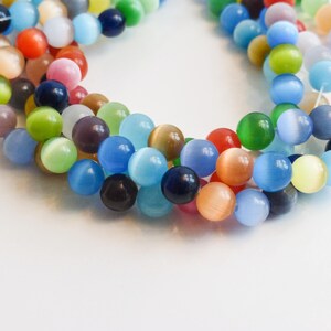 May include: A strand of colorful cat's eye beads, featuring a variety of shades of blue, green, yellow, orange, and red. The beads are round and have a smooth, glossy finish.