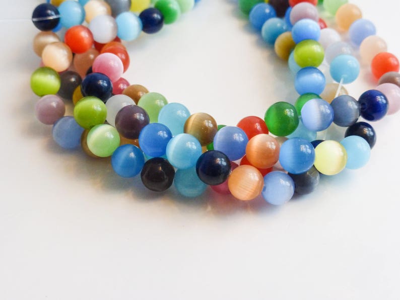 May include: A strand of colorful cat's eye beads, featuring a variety of shades of blue, green, yellow, orange, and red. The beads are round and have a smooth, glossy finish.