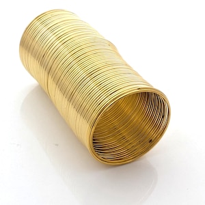 Puede incluir: Un brazalete dorado compuesto por numerosos anillos metálicos finos y enrollados. El brazalete cilíndrico parece estar hecho de un material brillante y reflectante. El diseño es simple y elegante, adecuado para varios estilos.