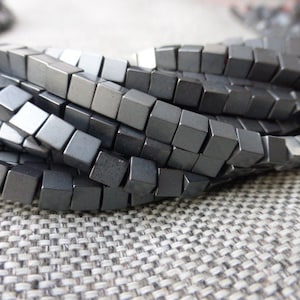 Peut inclure: Un brin de perles carrées de couleur gris foncé. Les perles sont en hématite et sont enfilées sur un fil transparent.