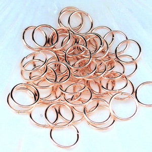 Op de afbeelding: Een stapel roségouden springringen, een soort sieraadbevestiging die wordt gebruikt om kettingen, bedels en andere sieraadcomponenten te verbinden.
