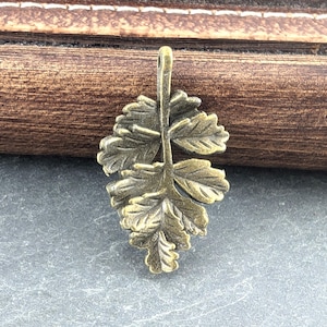 May include: A gold-toned metal leaf charm with a detailed design. The charm is ideal for adding a touch of nature to jewellery or crafts.
