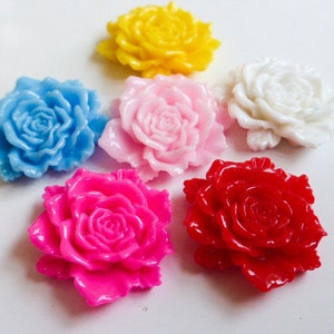 May include: Six colourful plastic rose flower embellishments. The flowers are in shades of pink, red, yellow, blue, and white.