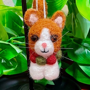 May include: A felt cat ornament with a white face, orange and white fur, and a red and green scarf. The cat has a pink nose and brown eyes.