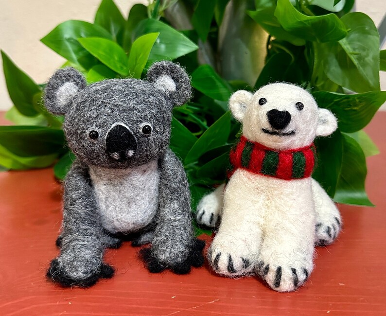May include: A grey koala and a white polar bear plush toy. The koala has a black nose and black eyes. The polar bear has a red and green striped scarf around its neck.