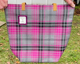May include: A pink and gray plaid tote bag with brown leather handles. The bag has a small purple patch with the text "PPG" on it.