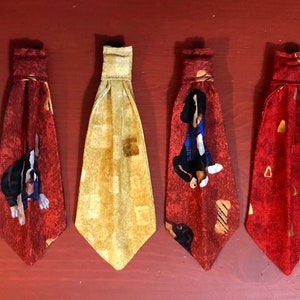 May include: Six different dog bow ties, each with a unique pattern. The bow ties are made of fabric and have a red, white, and green color scheme. The bow ties are all tied around a white string.
