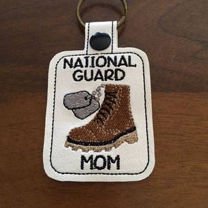 May include: White leather keychain with a brown boot, two silver dog tags, and the text "National Guard Mom".