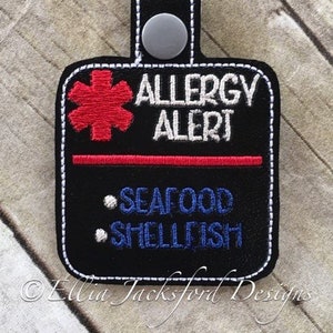 Può includere: Portachiavi nero di allerta allergia con una stella della vita rossa e testo bianco che recita "Allergia Alert" e "Frutti di mare, Crostacei".