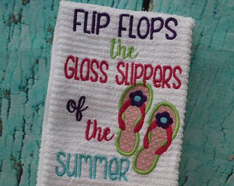 May include: White kitchen towel with embroidered text "Flip Flops the Glass Slippers of the Summer" and a pair of pink and green flip flops.
