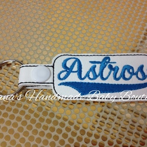 May include: White leather keychain with a blue and white embroidered "Astros" logo. The keychain has a silver metal ring.