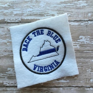 Pode incluir: Etiqueta bordada com um círculo preto e o texto "Back the Blue Virginia" em branco. Dentro do círculo, há um contorno do estado da Virgínia com uma linha azul que o atravessa.