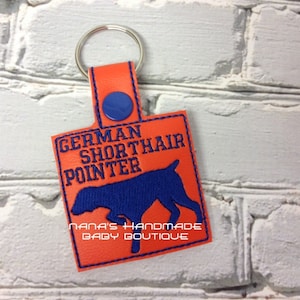May include: Orange leather keychain with a blue embroidered German Shorthaired Pointer silhouette and the text "GERMAN SHORTHAIR POINTER" and "NANA'S HANDMADE BABY BOUTIQUE".