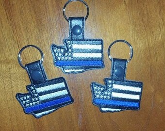 Puede incluir: Tres llaveros de cuero negro con un diseño de bandera estadounidense de línea azul en forma del estado de Washington.