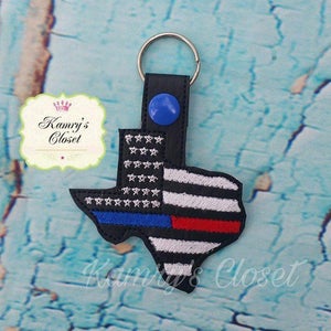 May include: A black leather keychain shaped like the state of Texas with a thin blue line, a thin red line, and an American flag design. The keychain has a silver key ring.