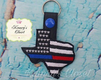 Puede incluir: Un llavero de cuero negro con forma del estado de Texas con una línea azul fina, una línea roja fina y un diseño de bandera estadounidense. El llavero tiene un anillo de llave plateado.