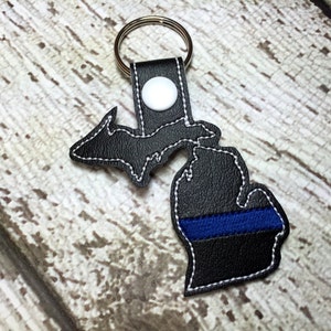 May include: Black leather keychain shaped like the state of Michigan with a blue thin blue line across the bottom.