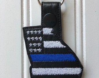Puede incluir: Llavero de cuero negro con un diseño de bandera estadounidense de línea azul. La bandera tiene estrellas y rayas blancas, una franja azul y una fina línea azul.
