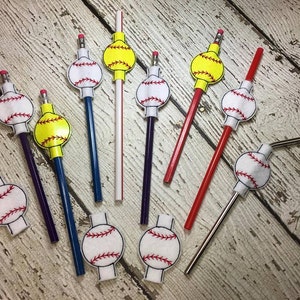 May include: A collection of eight baseball and softball themed pencil toppers and straw toppers. The toppers are made of felt and feature a white baseball or softball with red stitching and a yellow softball with red stitching. The toppers are attached to pencils and straws of various colors.