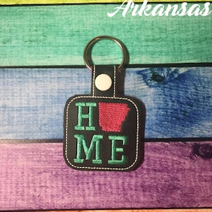 May include: A black leather keychain with a green embroidered "HOME" with the state of Arkansas in red in the middle of the word. The keychain has a silver key ring.
