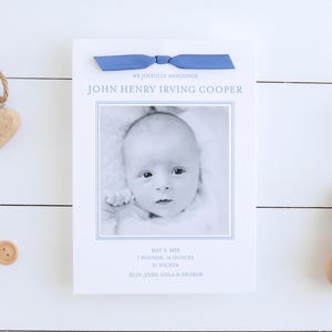 May include: A white card with a blue ribbon announcing the birth of John Henry Irving Cooper. The card includes a black and white photo of the baby, the date of birth, weight, and length. The card also includes the names of the baby's siblings: Elly, John, Lola, and George.